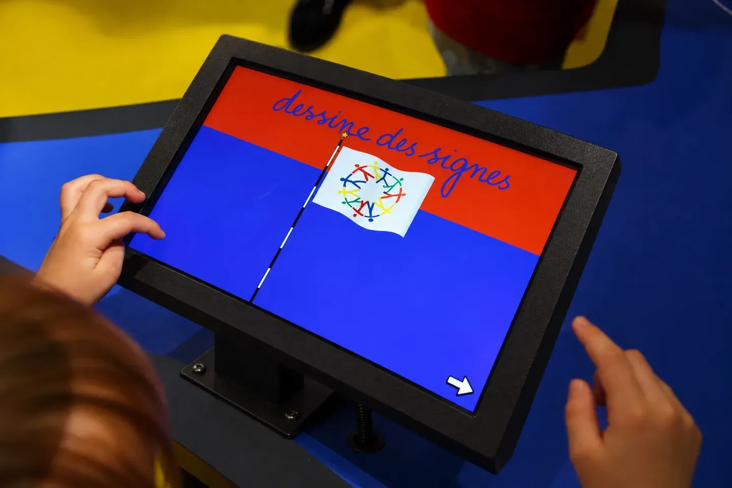 Un enfant dessine sur la borne tactile « Dessine des signes » : un drapeau rouge et bleu à colorier.